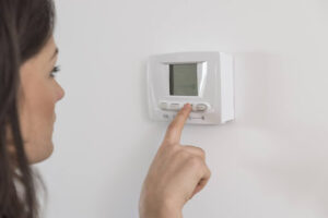 A woman adjusting a thermostat in a home.